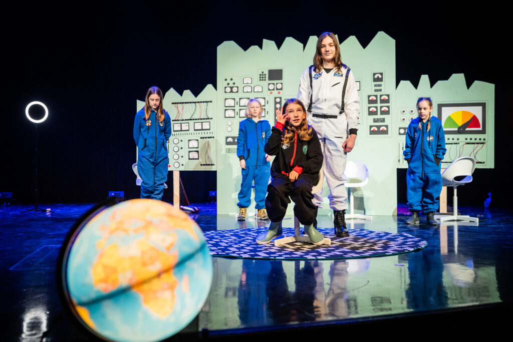 Dans la pièce Zoey et les luciens, on remarque des éléments de mise en scène : un panneau de contrôle au centre de la scène, un projecteur allumé à l’avant-scène et, de plus, les comédiens s’adressent au public plutôt que l’un à l’autre.